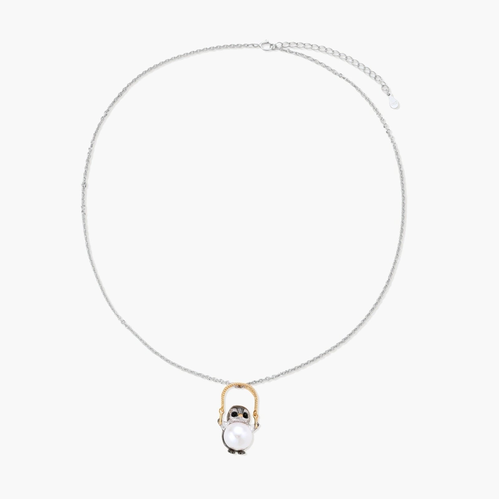 Whimsical owl pendant holding a white pearl on a gold swing, rhodium-plated silver chain on cream background.