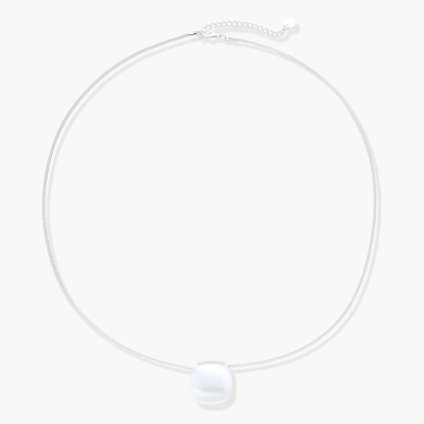 Minimalist brushed sterling silver dome pendant on delicate chain against cream background, showing matte textured finish