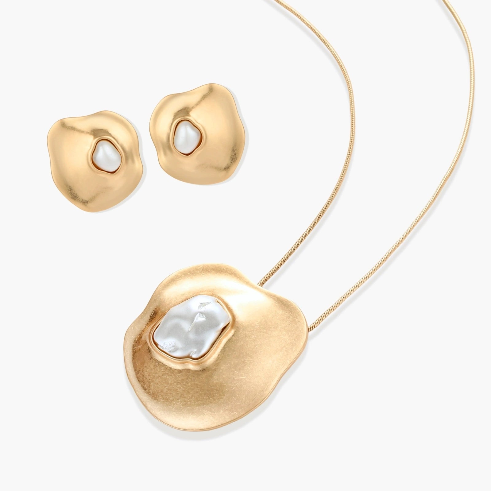 Close-up of organic gold-toned earrings and necklace with white baroque pearls on neutral background.