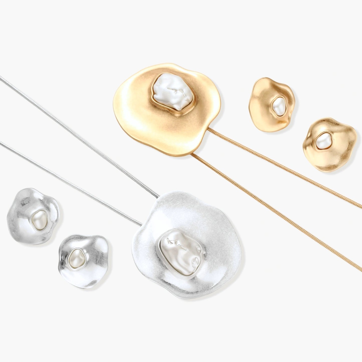 Close-up of organic gold-toned earrings and necklace with white baroque pearls on neutral background.